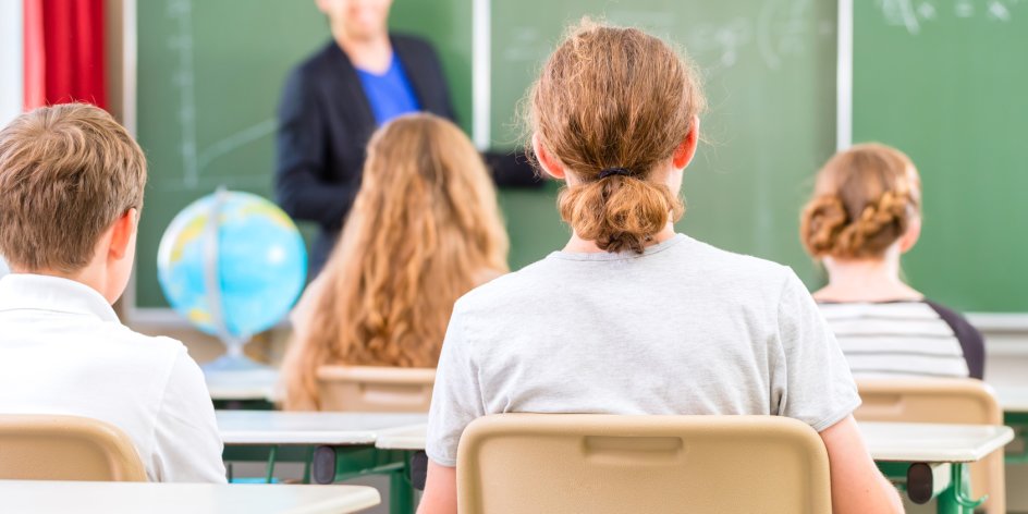 Ein Lehrer steht an einer Tafel vor einer Schulklasse.