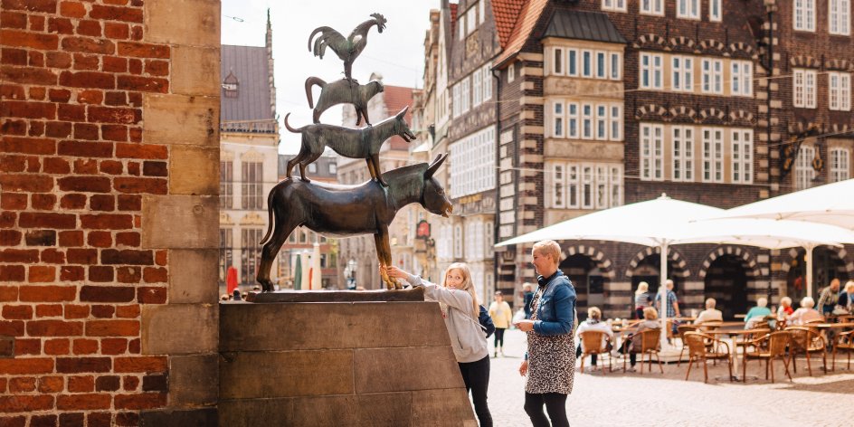 A girl and a woman stand in front of the Bremen Town Musicians.