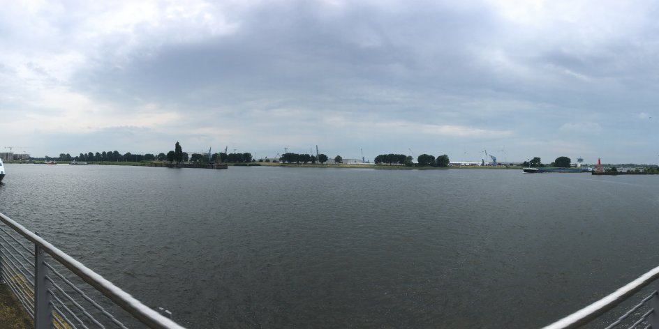 Zu sehen ist eine große, dunkle Wasserfläche. Im rechten und linken Teil des Bildes ist ein Metallgeländer zu erkennen. Links legt ein Boot an. 