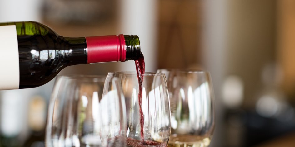 Drei gefüllte Weingläser, eine Flasche gießt Rotwein in eines der Gläser.