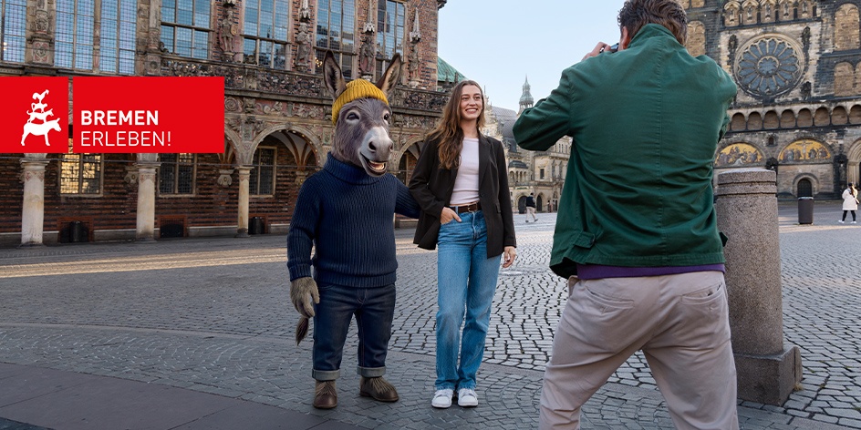 Eine künstlich generierte, vermenschlichte Esel-Figur posiert neben einer jungen Frauen für einen Fotografen vor dem Bremer Rathaus