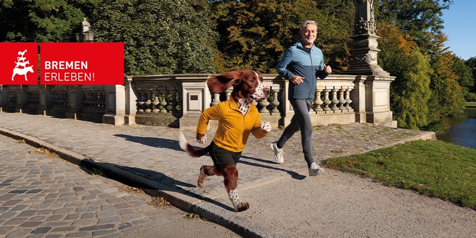 Eine künstlich generierte, vermenschlichte Hunde-Figur joggt neben einem Mann durch den Bürgerpark Bremen