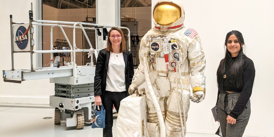 Zwei Wissenschaftlerinnen neben einem NASA-Astronatuenkostüm
