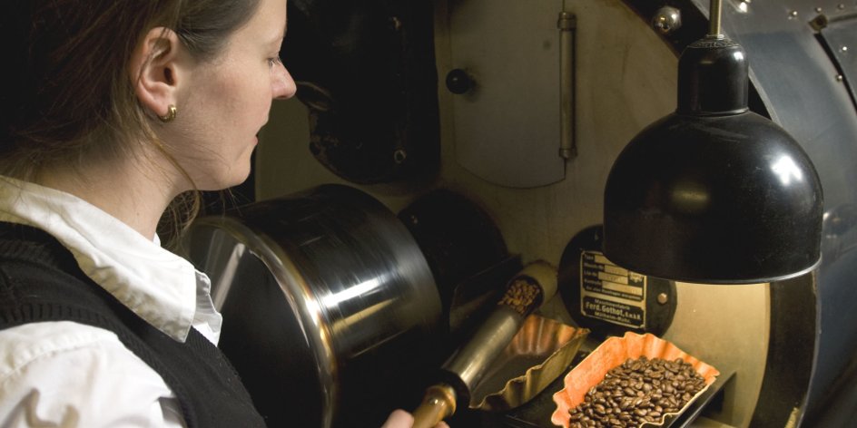 Eine Frau nimmt Kaffeebohnen aus einer großen Maschine.