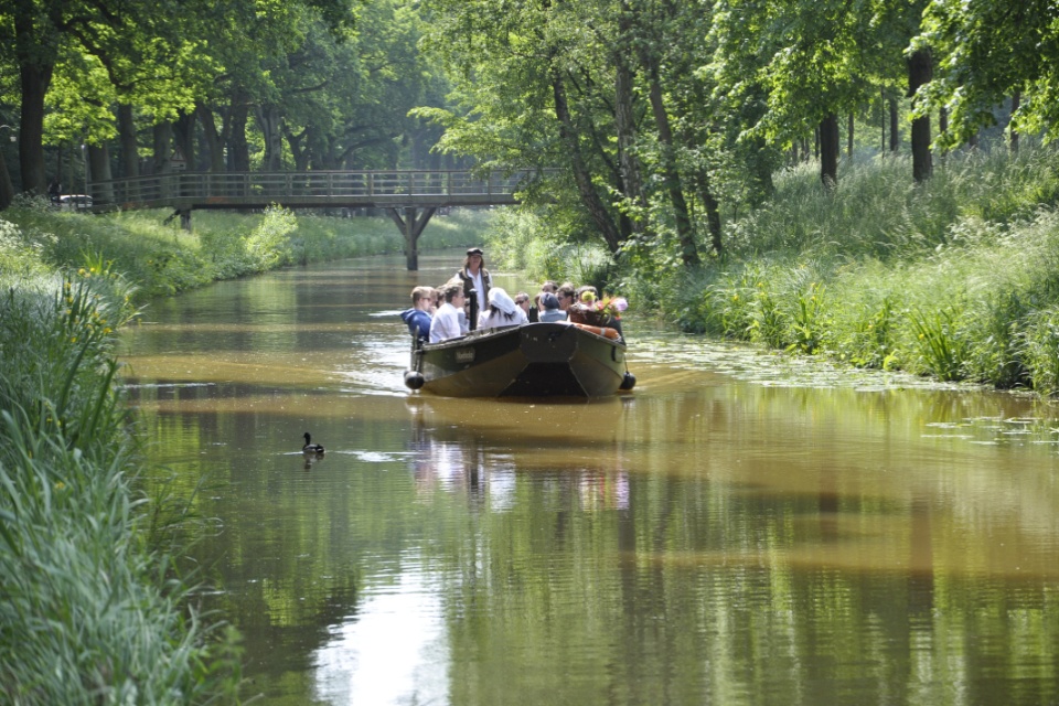 Eine Gruppe Menschen fährt mit einem Torfkahn einen Fluss entlang