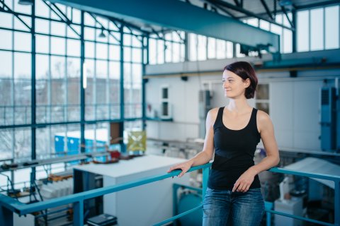 Eine Frau lehnt an einem Geländer und steht oberhalb einer Halle.
