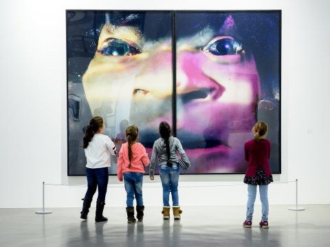 Vier junge Mädchen stehen vor einem bunten Bild mit einem verzerrten Gesicht. 