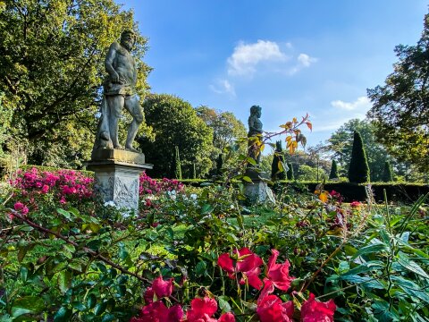Zwei Skulpturen stehen in einem Rosenbeet.