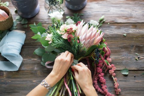 Frauenhände binden einen bunten Blumenstrauß zusammen.