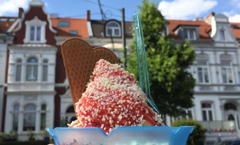 Ein Spaghetti Eis mit einer Waffel in einem blauen Becher wird in der Wachmannstraße bei Eis Molin hochgehoben.