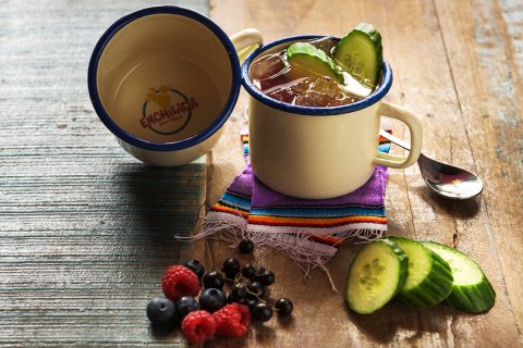 Ein Cocktail namens Enchilada Mule, serviert im Becher. Davor Früchte und Gurken.