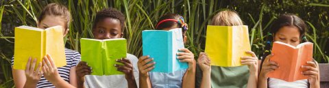 5 lesende Kinder auf einer Bank im Grünen