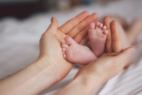 Die Hände einer Erwachsenen umfassen die Füße eines Babys