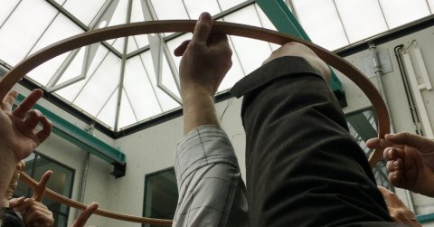 Ein großer Holzring von von vielen Zeigefingern in die Höhe gehalten