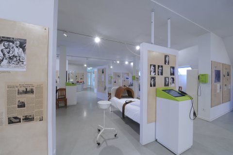 Eine Innenaufnahme aus dem hellen Krankenhausmuseum. Zu sehen sind einige Ausstellungsstücke sowie schwarz-weiß Bilder und Infotexte.