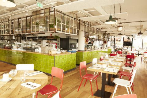 Die Innenräume eines großen Restaurants mit grün gefliester Theke und zahlreichen gedeckten Tischen.