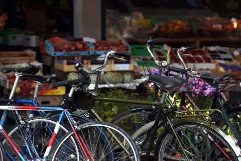 Parkende Fahrräder, im Hintergrund ein Obst- und Gemüsegeschäft mit Warenkörben vor dem Fenster.