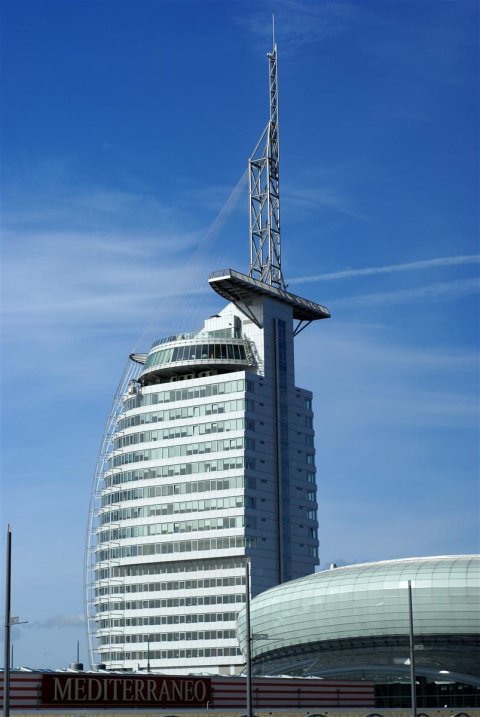 Ein mehrstöckiges Gebäude mit einer Spitze. Im Hintergrund ist blauer Himmel zu sehen.