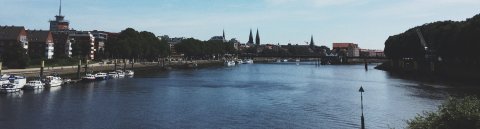 Der Ausblick auf einen Fluss, Häuser und einer weiteren Brücke im Hintergrund. Schiffe liegen an der Seite