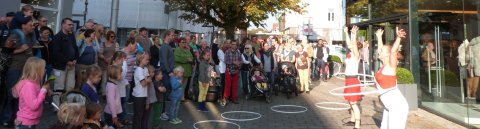 Eine größere Menschen Gruppe steht im Halbkreis um zwei Straßenkünstlerinnen in Vegesack, die eine Hula-Hoop-Nummer zeigen.