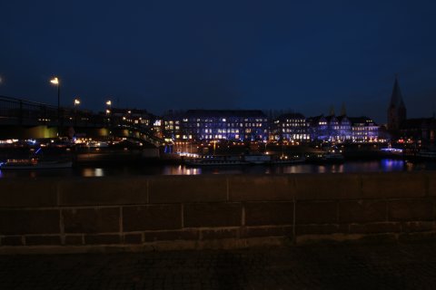 Blick über die Mauer auf die Weser am Abend mit beleuchteten Häusern