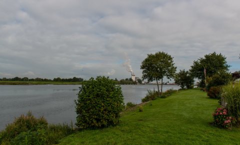 Ein Blick vom Ufer auf die Weser, im Hintergrund raucht der Schornstein eines Unternehmens.