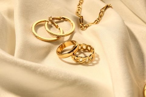 Goldene Ohrringe, Ringe und eine Kette auf einem weißen Tuch.