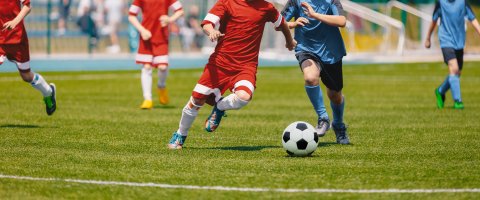 Personen in roten und blauen Trikots spielen Fußball. Ihre Köpfe sind nicht auf dem Bild zu sehen. 