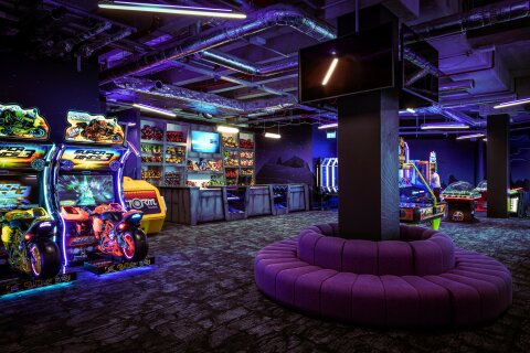 Die Arcade von innen. Bunte Spielautomaten stehen an der Wand. In der Mitte ist eine Sitzgelegenheit
