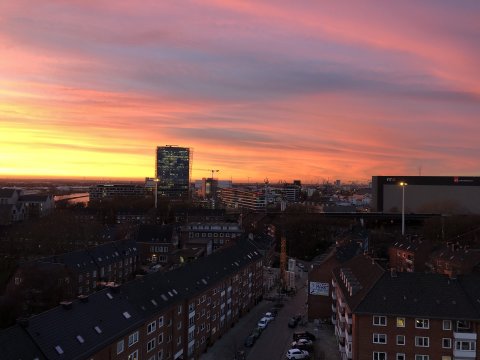 Die Aussicht von oben auf eine Straße und Häuser vor einem pink gefärbtem Himmel.