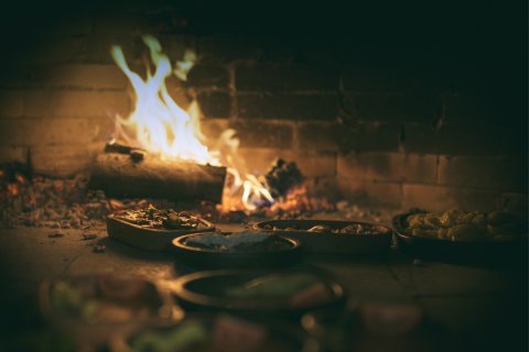 Schälchen mit anatolischen Spezialitäten im Lehmofen, im Hintergrund Feuer.