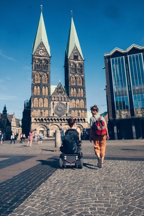 Two women on Bremen's market square. They are looking at the cathedral and talking. One of them is sitting in a wheelchair.