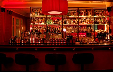 Eine Innenaufnahme der Lemonlounge in einem Rotorangenlicht seht ihr eine gut gefüllte Cocktailbar.