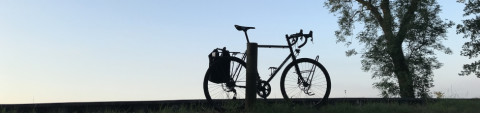 Ein Fahrrad steht auf einem Hügel abgestellt neben einem Baum vor blauem Himmel