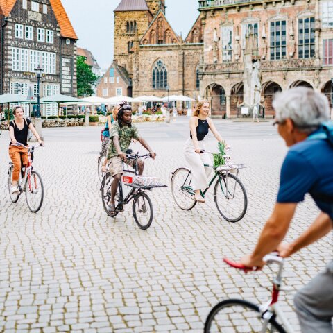 Eine Gruppe von jungen Radfahrerinnen und Radfahrern fährt über den Marktplatz. Im Hintergrund sind das Rathaus und die Liebfrauenkirche zu sehen