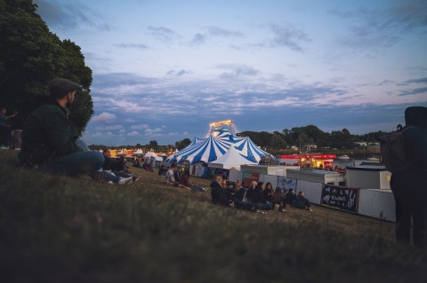 Menschen sitzen am Osterdeich in der Abenddämmerung und blicken aus die Festzelte der Breminale.