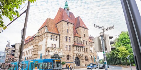 Außenaufnahme der Stadtbibliothek Bremen. Das Gebäude befindet sich an einer Kreuzung. Eine Straßenbahn und Autos fahren vorbei. 