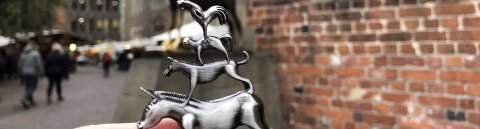 Eine Hand, die eine Metallfigur der Bremer Stadtmusikanten vor die echte Bronzefigur der Bremer Stadtmusikanten hält.