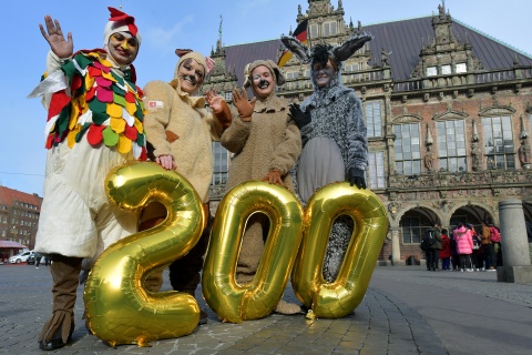Die Stadtmusikanten springen mit einer großen goldenen 200 vor dem Bremer Rathaus in die Höhe.