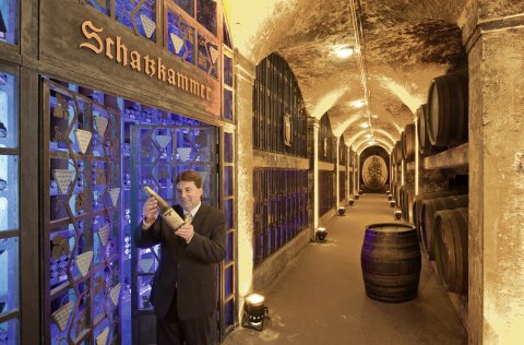 Ein Kellner hält eine Flasche Wein in den Händen. Er steht in der Schatzkammer des Bremer Ratskellers. Im Hintergrund sind zahlreiche Weinfässer zu sehen. 