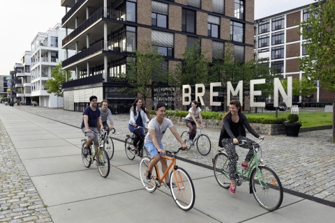 Eine Gruppe junger Leute fährt mit dem Fahrrad an dem Wort Bremen vorbei.