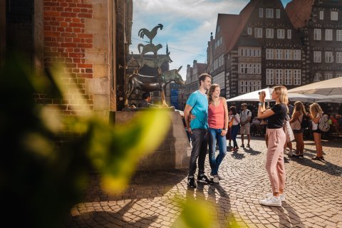 Ein Pärchen steht vor der Bronzestatue der Bremer Stadtmusikanten und lässt sich von einer Frau fotografieren.