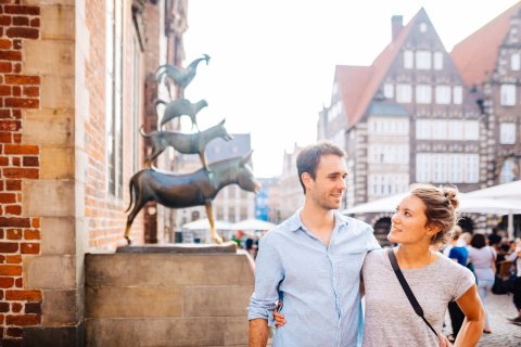 A woman and a man stand in front of the Bremen Town Musicians. 