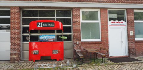 Der Eingangsbereich vom Straßenbahnmuseum in Sebaldsbrück. Zu sehen ist die Eingangstür mit Sitzgelegenheiten und der Front einer roten Straßenbahn
