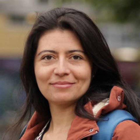 Das Portrait einer Frau mittleren Alters mit dunklen Haaren, die in die Kamera schaut.