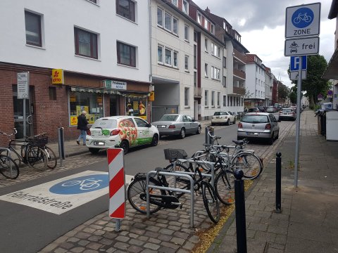 Ein Piktogramm auf dem Straßenbelag und die Beschilderung am Straßenrand weisen die Straße als Fahrradstraße und Teil einer Fahrradzone aus