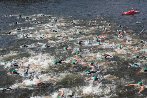 Triathlon-Teilnehmer schwimmen, während iim Hintergrund ein Kanufahrer treibt.