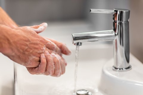 Zwei eingeseifte Hände an einem Waschbecken und ein Wasserhahn, aus dem Wasser läuft.