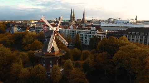 Eine Drohnenaufnahme der Mühle in Bremen umgeben von bunten Bäumen.