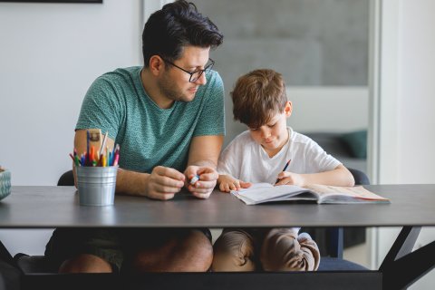 Ein Mann und ein Junge sitzen am Tisch und machen gemeinsam Hausaufgaben.